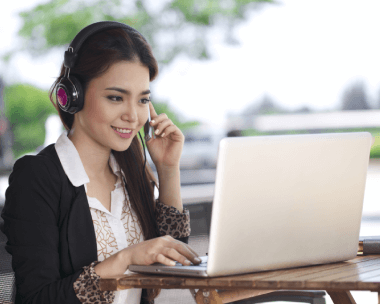 Young Asian woman working on a laptop in a coffee shop, highlighting efficiency in Chinese transcription services.